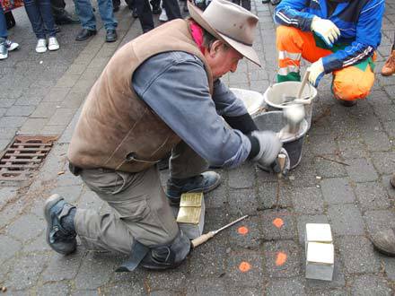 Das Foto zeigt den Künstler am Boden kniend bei der Entnahme der herkömmlichen Pflastersteine